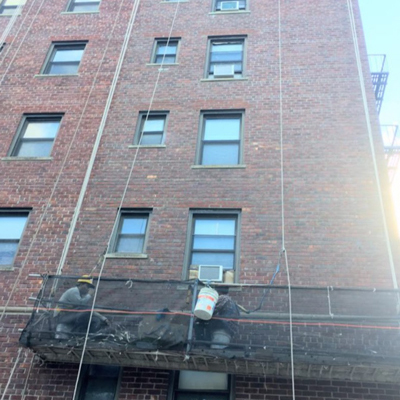 A man is focused on his work while seated at a balcony, surrounded by the urban landscape of a building.