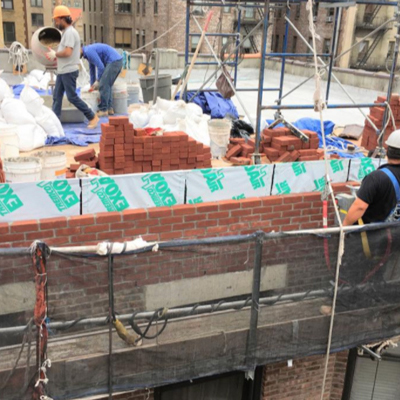 Construction workers on a roof diligently building a brick wall under clear blue skies, showcasing teamwork and craftsmanship.