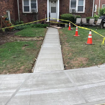 A construction worker lays concrete for a new sidewalk in front of a residential house, enhancing the property’s accessibility.