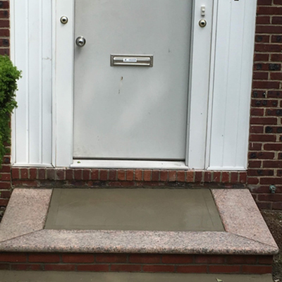 A cement step leading up to a door, showcasing a sturdy entrance with a simple, functional design.